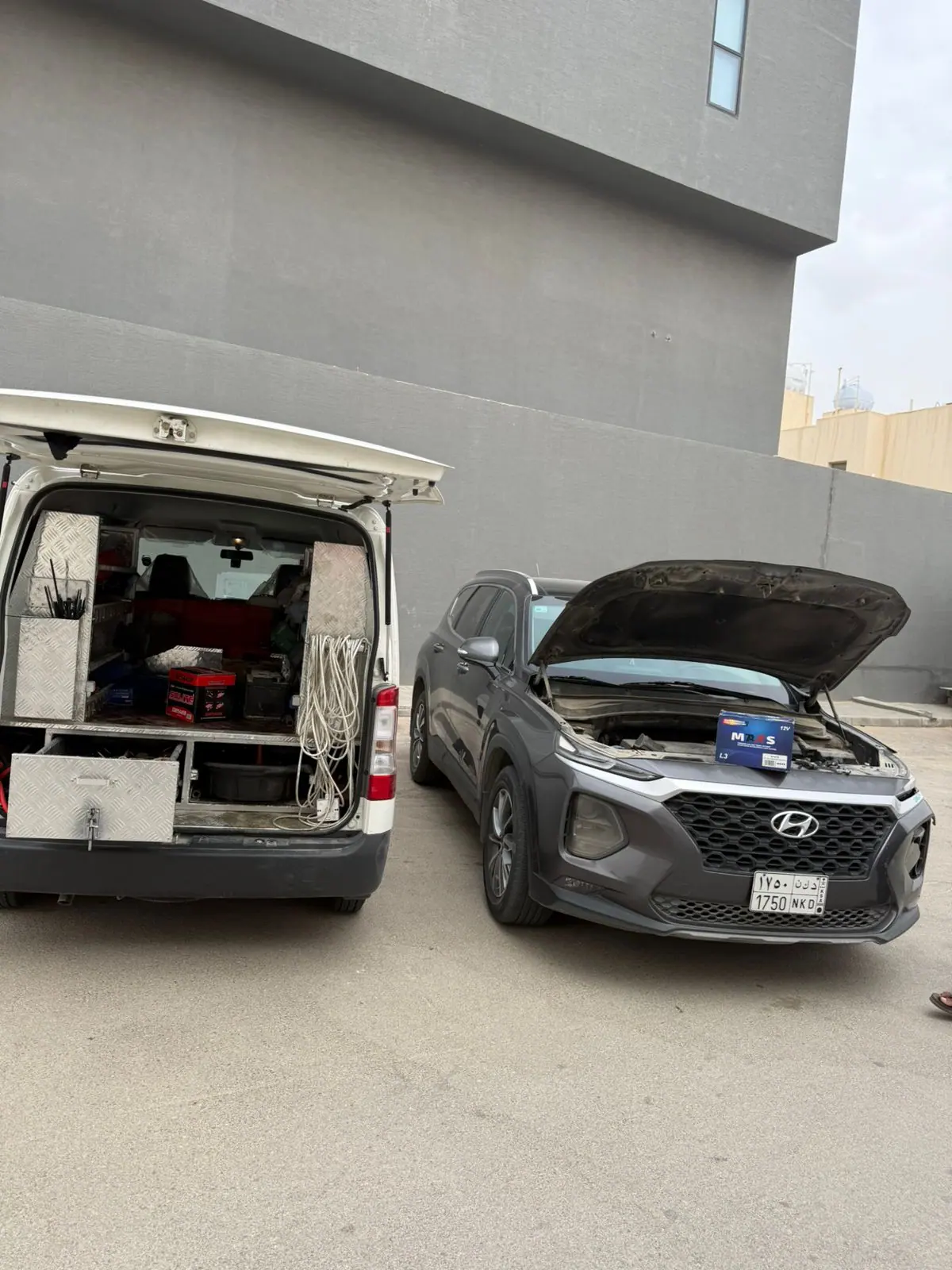 A new car battery on the engine bay of a Hyundai Santa Fe beside the Saaed Service van in Riyadh