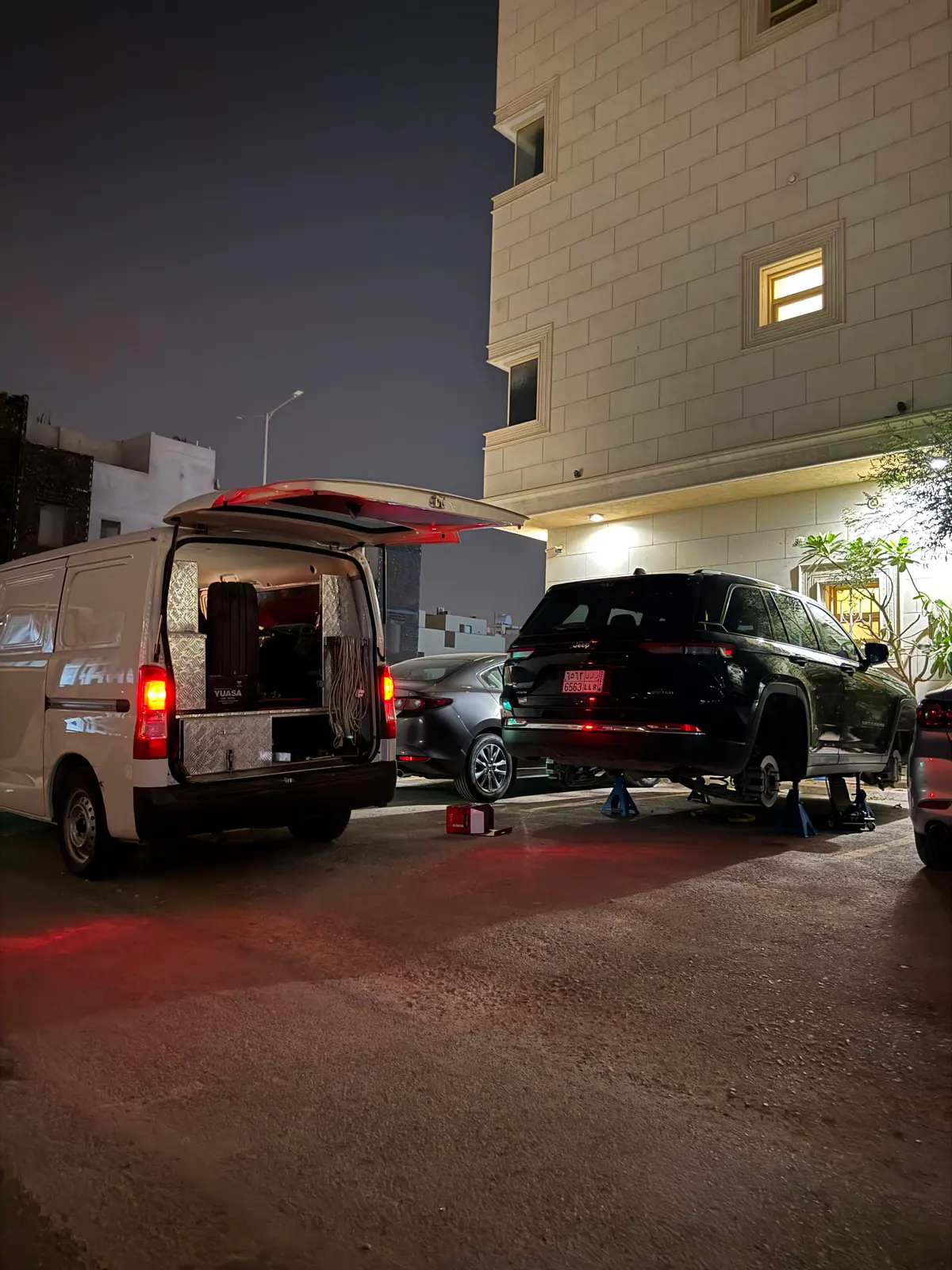 A black Jeep Grand Cherokee raised on four axle stands for brake work at night in Riyadh