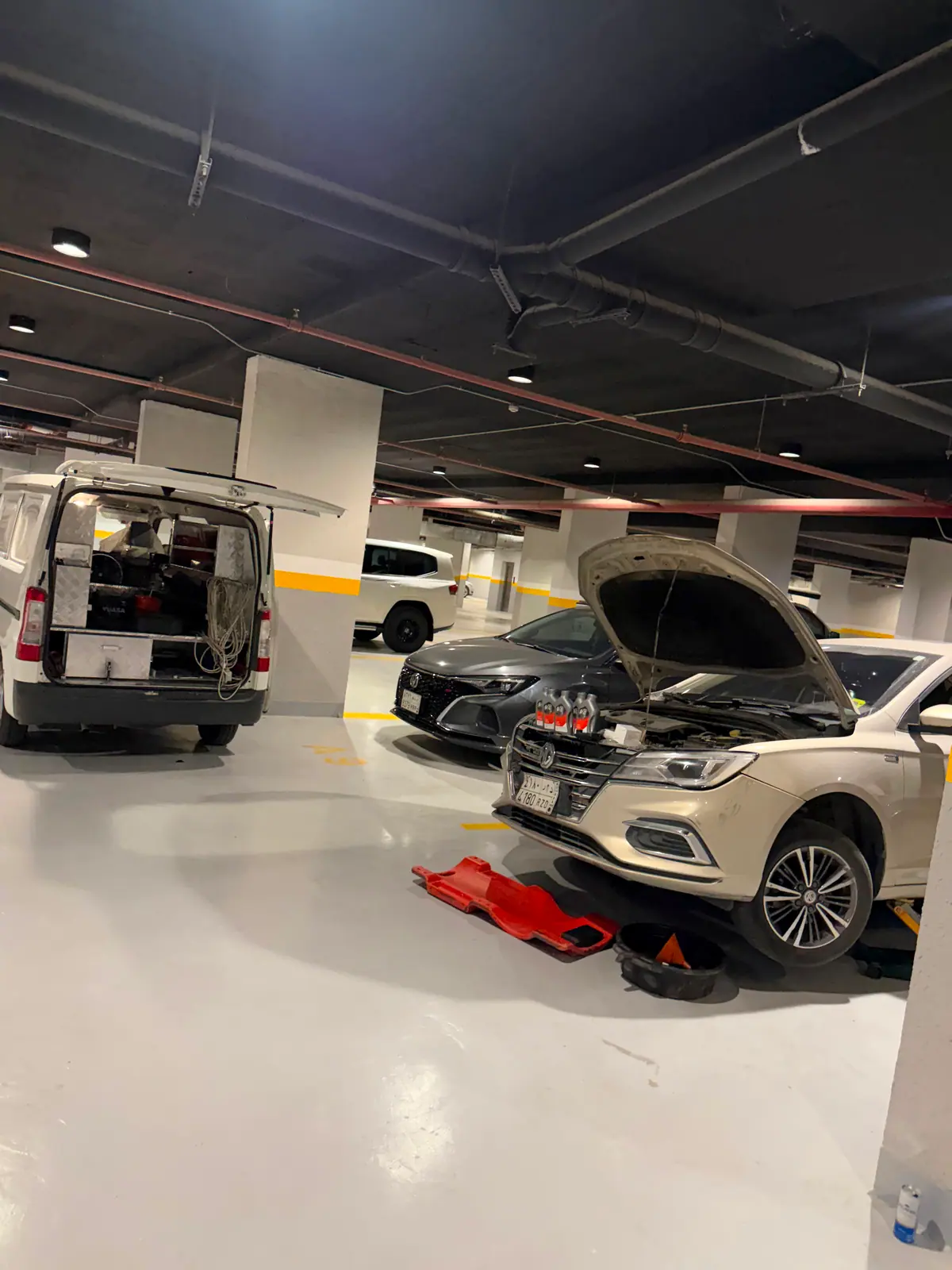 Mobile oil and filter change in a Riyadh car park — fresh oil bottles and a drain pan beside the Saaed van