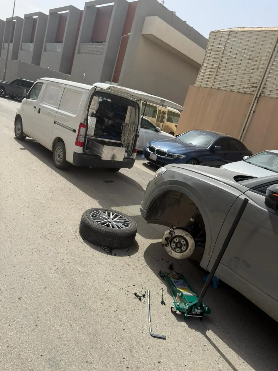 Mobile tyre change in Riyadh — an SUV raised on a trolley jack with the alloy wheel off beside the Saaed Service van